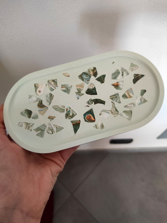 svuotatasche note di verde e marmo: vassoio ovale artigianale in resina ecologica verde pallido. La superficie interna presenta un motivo a terrazzo con frammenti di marmo marmorizzati nei toni del verde scuro, marrone e oro.