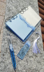 Set da cancelleria in resina artigianale a tema mare con effetto onde blu e schiuma bianca, composto da un taccuino con anelli metallici, una penna e un segnalibro 
