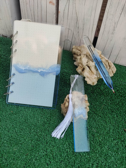 Set da cancelleria in resina artigianale a tema mare con effetto onde blu e schiuma bianca, composto da un taccuino con anelli metallici, una penna e un segnalibro 