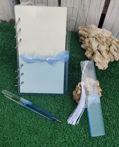 Set da cancelleria in resina artigianale a tema mare con effetto onde blu e schiuma bianca, composto da un taccuino con anelli metallici, una penna e un segnalibro 