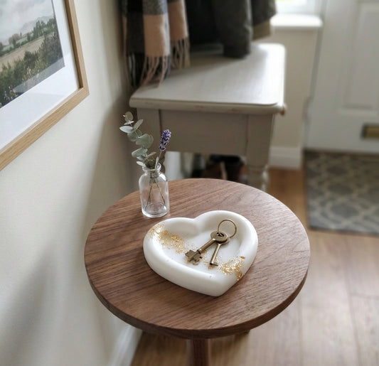 Svuotatasche artigianale a forma di cuore in resina bianca con rifinitura liscia, appoggiato su un piano in legno. L'interno del piatto è decorato con una striscia di dettagli in foglia oro frantumata che attraversa la superficie.