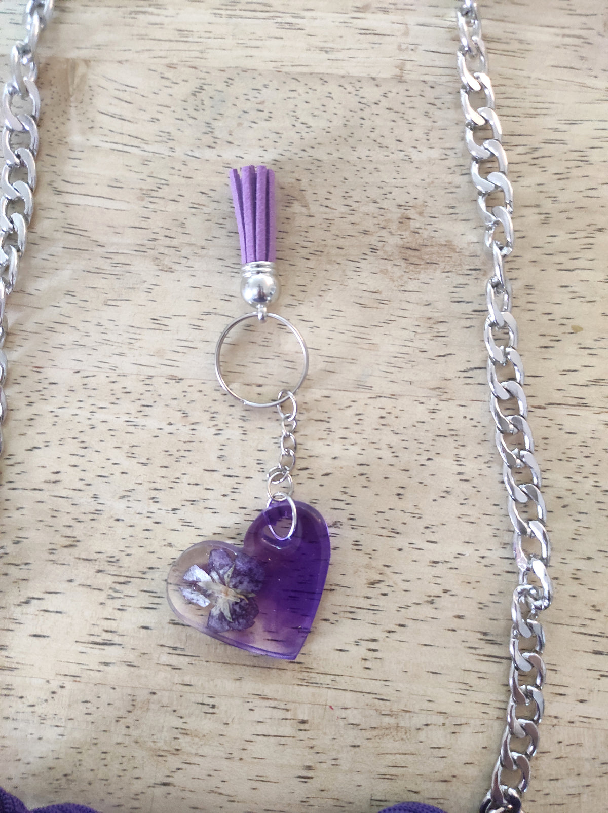 Borsa artigianale all'uncinetto a forma di cuore di colore viola inteso, con manico intrecciato e tracolla in catena metallica argento. Abbinato un portachiavi a forma di cuore in resina viola con fiori secchi e nappa lilla. 