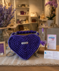 Borsa artigianale all'uncinetto a forma di cuore di colore viola inteso, con manico intrecciato e tracolla in catena metallica argento. Abbinato un portachiavi a forma di cuore in resina viola con fiori secchi e nappa lilla. 